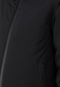 Black puffer jacket with a smooth texture, featuring a zippered front and side pockets. Includes stitching details along the seams.