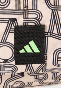 Μαύρο υφασμάτινο έμπλαστρο με τρεις πράσινες διαγώνιες ρίγες πάνω σε μπεζ ύφασμα με σχέδιο από γράμματα με μαύρο περίγραμμα.