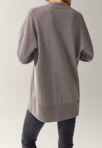 Szary, oversize sweter o teksturowanym splocie, z opadającymi ramionami i ściągaczem u dołu, w połączeniu z czarnymi dopasowanymi spodniami.