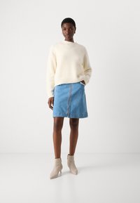 Kremfarget fluffy genser og blå denimskjørt med frontglidelås, kombinert med beige ankelstøvletter. Fokuser på avslappet passform og tekstur.