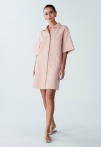 Krótka sukienka koszulowa w różowym kolorze o prostym kroju, z krótkimi rękawami i przednimi kieszeniami, zapinana na guziki i o gładkiej fakturze.