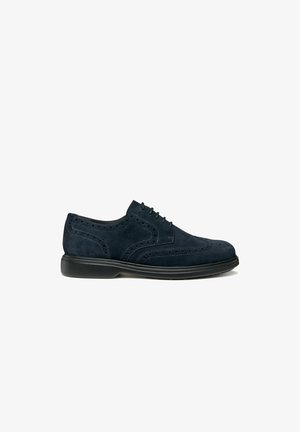 Scarpe da uomo in suede blu navy, modello brogue, con suola nera, chiusura con lacci e perforazioni decorative sul lato e sulla punta.