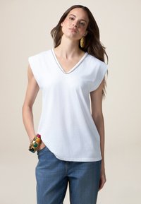 T-shirt bianca in cotone con scollatura a V e maniche corte, con un accento argento lungo la scollatura. Abbinata a jeans denim blu.