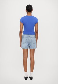 T-shirt blu attillata, maniche corte, abbinata a pantaloni corti in denim blu chiaro. Design minimalista con una texture liscia, indossata con calzini bianchi e scarpe nere.