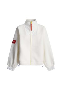 Λευκό φλις μπουφάν με ψηλό γιακά, κίτρινο φερμουάρ και ελαστικές μανσέτες. Διαθέτει κόκκινο έμπλαστρο στο αριστερό μανίκι και μπλε κορδόνια για ρυθμιζόμενο σφιξίμο.