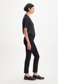 Zwarte short-sleeve shirt met twee borstzakken, gecombineerd met zwarte slim-fit jeans en zwarte loafers, weergegeven in een zijprofiel.