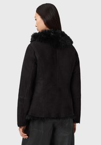 Giacca in camoscio nero con colletto in pelliccia sintetica. Caratterizzata da una vestibilità sagomata, maniche lunghe e finitura testurizzata.