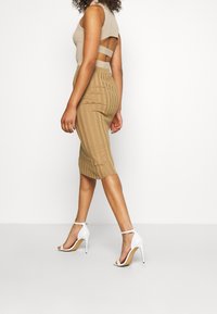 Pletený béžový top s výřezy na ramenech, kombinovaný s žebrovanou béžovou tužkovou sukní. Nosený s bílými sandály na vysokém podpatku.