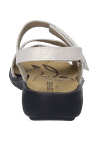 White leather sandal with multiple straps, a cushioned beige insole, and a black rubber sole. Minimalistic design with decorative detailing.