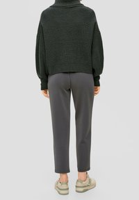 Ciemnozielony sweterek z dzianiny o kroju cropped z szerokimi rękawami, zestawiony z szarymi spodniami w tapered i beżowymi trampkami. Miękka tekstura i luźny fason.