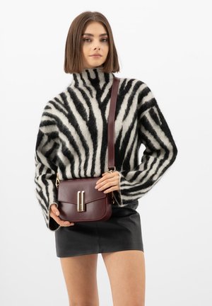 Vrouw draagt een zwart-wit gestreepte, zachte trui, een zwarte leren minirok, en houdt een donker bordeauxrode leren crossbodytas met gouden sierbeslag vast.