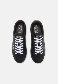 Czarne skórzane sneakersy z białymi sznurówkami, z logo na języku i boku oraz teksturowaną gumową podeszwą. Płaski fason, okrągły czubek.