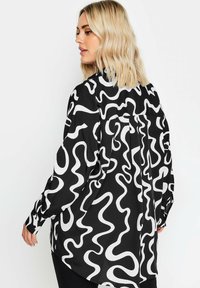 Maglietta a maniche lunghe in bianco e nero con un motivo astratto ondulato, realizzata in tessuto morbido, con un dettaglio a pieghe sul retro.
