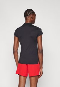 Μαύρο πόλο μπλουζάκι με κοντά μανίκια και γιακά, συνδυασμένο με κόκκινες αθλητικές βερμούδες. Ο ιστός φαίνεται λείος με κομψό σχέδιο.