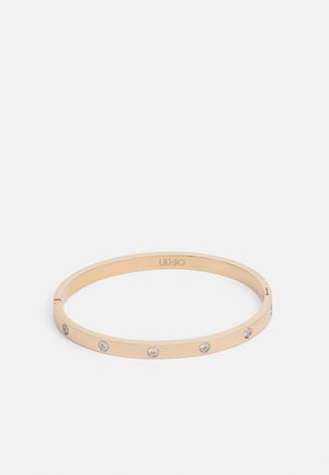 Zlato obarvana kovinska zapestnica z gladko površino, s šestimi enakomerno razporejenimi prozornimi kristali po pasu, embosirano logotip na notranji površini.