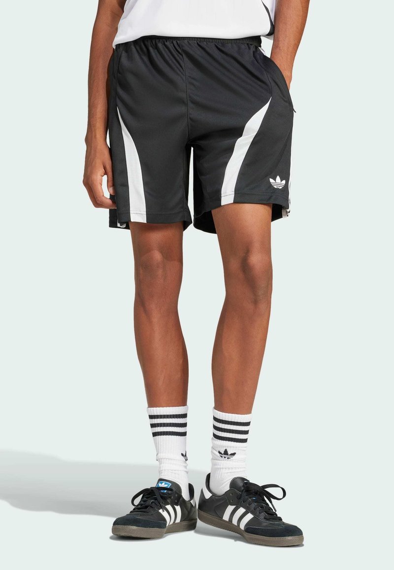 Shorts de sport noirs avec des rayures blanches sur les côtés, taille élastique et poches. Associés à des baskets noires et des chaussettes blanches rayées.
