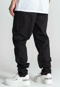 Joggers negros ajustados, hechos de una tela ligera, con cintura elástica y puños, combinados con zapatillas blancas con marca.