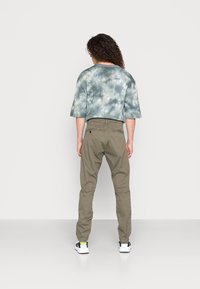 Světle modré tričko s krátkým rukávem s tie-dye vzorem, olivově zelené kalhoty, bílé tenisky s tmavě modrými detaily. Hladké textury, volný střih, neformální design.