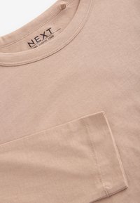 Beige long sleeve crew t-shirt made of soft cotton. Features a round neckline and a left chest pocket. Simple, clean design.