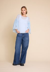 Lys blå, gjennomsiktig bluse med volangerm; parret med løst sittende blå denimjeans. Sorte fottøy fullfører antrekket.