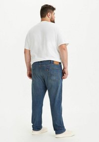 Valkoinen lyhythihainen t-paita, joka on yhdistetty sinisiin farkkuihin, joissa on suora leikkaus, viisi taskua ja nahkainen takapatch.