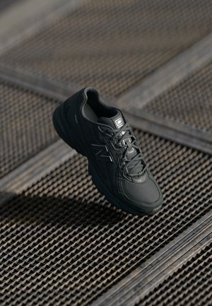 Zwarte sportieve schoen met een gestructureerde synthetische bovenkant, gevoerde zool en veters, geplaatst op een gemarmerd metalen oppervlak.