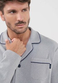 Camisa de pijama texturizada en gris con ribete azul marino, cuello con muesca, cierre de botones y un bolsillo con una etiqueta que dice "LOHE".