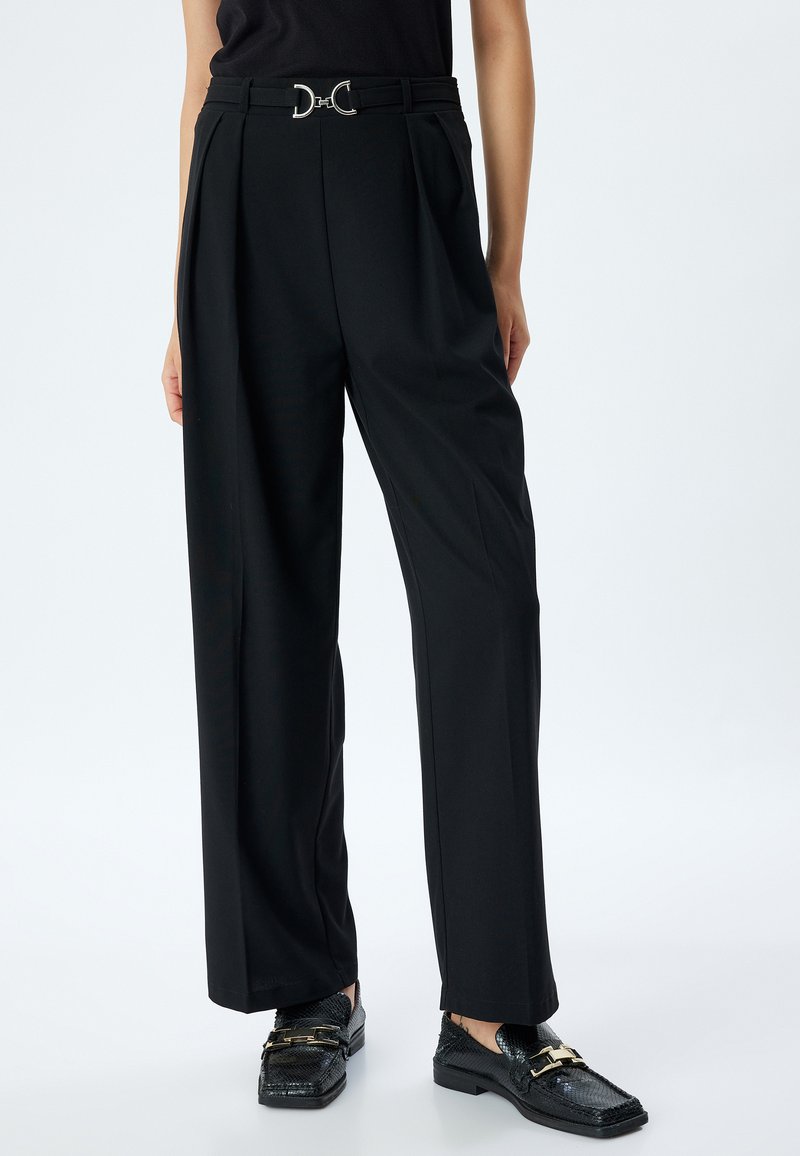 Pantalons noir ajustés avec une coupe large. Dotés d'une ceinture avec une boucle en D argentée. Tissu lisse avec une coupe structurée.
