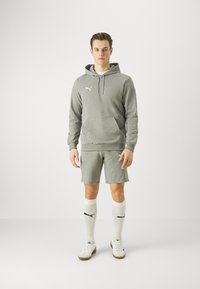 Felpa sportiva grigia con tasca a marsupio, pantaloni corti abbinati, calzini sportivi bianchi e sneaker bianche. Presenta il logo Puma in bianco.