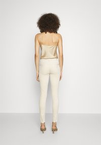 Camisola in satin beige e jeans skinny beige chiaro, con vita media e vestibilità slanciata, abbinati a scarpe con tacco a strappi.