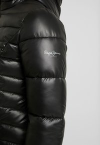 Černá péřová bunda s lesklým povrchem, s horizontálními švy a výrazným logem na rukávu. Navržena pro teplo a pohodlí.