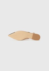 Escarpin nude à bout pointu avec un dessus en cuir lisse, un talon fin et une semelle en caoutchouc texturé. Accent noir sur la cap-toe.