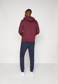 Bordeaux hoodie met een kangoeroezak en marineblauwe joggers. Heeft ribgebreide manchetten en zoom. Witte sneakers maken de outfit af.
