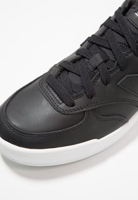 Baskets en cuir noir à finition lisse, avec une semelle en caoutchouc blanche et des lacets noirs. Le design comprend des coutures discrètes et des accents subtils.