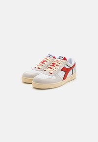 Hvite og grå sneakers med røde og svarte detaljer, laget av lær og semsket skinn, med perforerte detaljer og beige gummisåler.