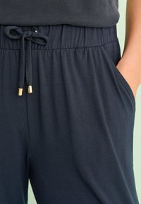 Joggers azul marino oscuro con cintura elástica, cordón con puntas doradas y bolsillos laterales. Tejido suave y liso. Corte casual.