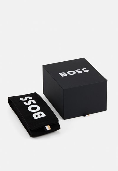 Черна подаръчна кутия с текста "BOSS" в бяло. До нея има черен несесер със същото брандиране, включващ малък акцентен етикет.