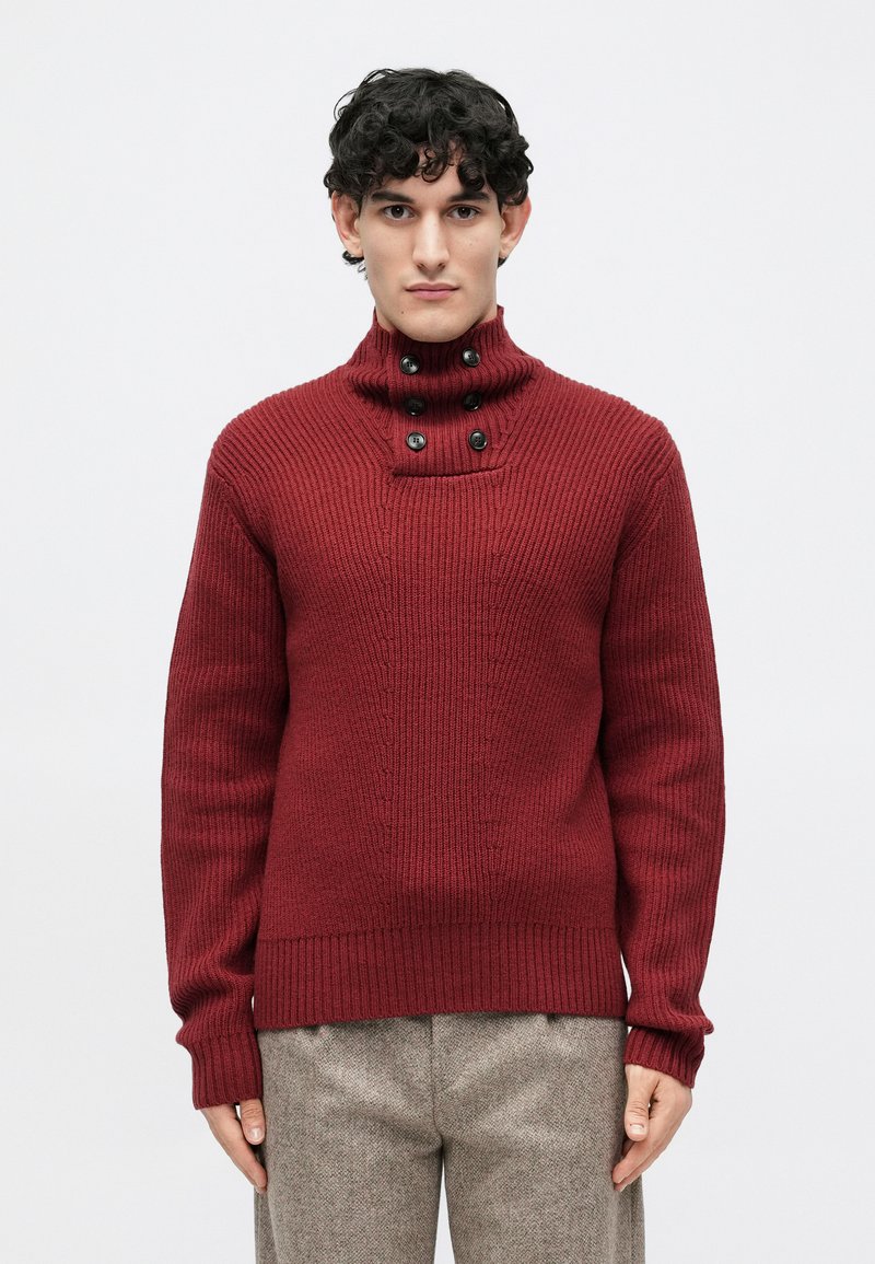 Burgundy knit sweater with a high collar, featuring button accents and ribbed cuffs and hem, displayed on a model against a plain background.