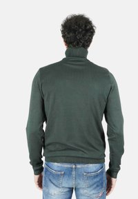 Maglione a collo alto verde lavorato a maglia con design aderente e trama a coste. Abbinato a jeans in denim azzurro chiaro, visto da dietro.