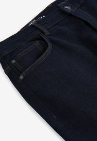 Donkerblauwe denim jeans met zichtbare tailleband, voorzak met muntzakje, riemlussen en metalen knoopsluiting met contrasterende stiksels.