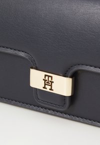 Marineblå lærwallet med en gullfarget lås med preget logo. Glatt tekstur med synlige sting og avrundede hjørner.