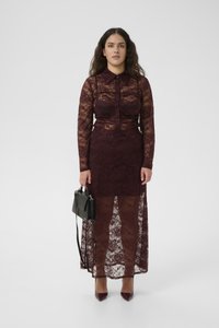 Lacekjole i burgunder med lange ermer, knaplukning foran og en gennemsigtig skørt. Accessoriseret med en sort håndtaske. Skoene er stiletter med spidse tæer.