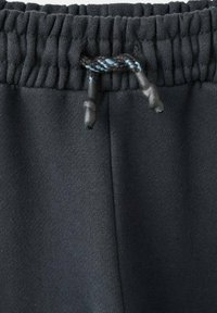 Close-up van een zwarte elastische tailleband met een zwart en blauwe trekkoord op donkere stofbroeken.