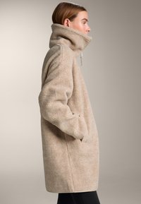 Beige, gezellige jas met een hoge kraag, een geborstelde buitenkant, zijzakken en lange mouwen, uitgevoerd in een ontspannen, oversized model.