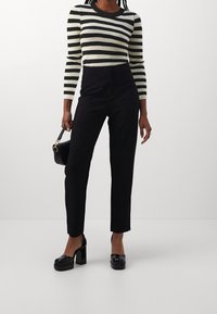 Czarne spodnie o wysokim stanie zestawione z długim rękawem topem w paski w kolorze czarnym i kremowym, podkreślone masywnymi czarnymi platformami.