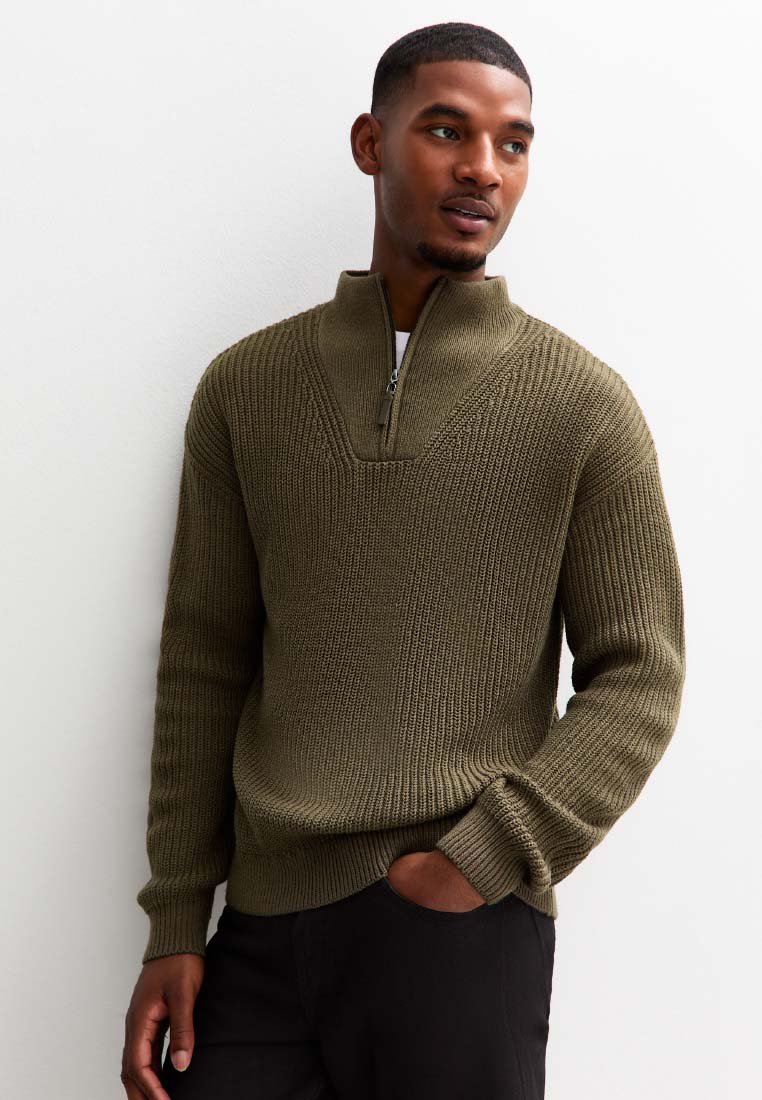 Olivgrön stickad tröja med dragkedja och ribbad textur samt ett chevronmönster vid bröstet. Långa ärmar och åtsittande nederkant.