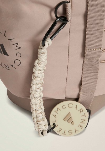 Light pink fabric bag with a black carabiner and a braided strap, featuring a cream circular tag with embossed logo. Smooth texture.