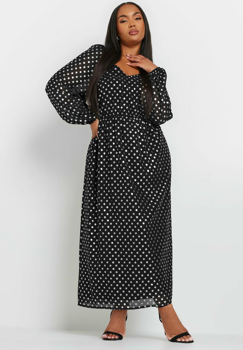 Musta pilkullinen maksimekko, jossa on pitkät, läpikuultavat puffihihat, joustava vyötärö ja V-mallinen kaula-aukko. Kangas on kevyttä ja virtaavaa.