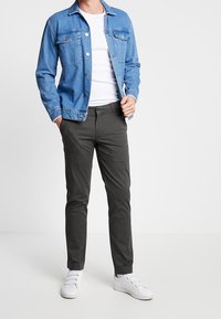 Niebieska dżinsowa kurtka z dwiema kieszeniami na piersi, noszona na białej koszulce, w połączeniu z ciemnoszarymi spodniami i białymi trampkami. Prosty, casualowy design.