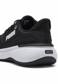 Zwarte sportieve schoen met een bovenwerk van mesh en een wit logo. Heeft een uitgesproken hiel en een getextureerde zool met het label "SOFTRIDE." Minimalistisch ontwerp.